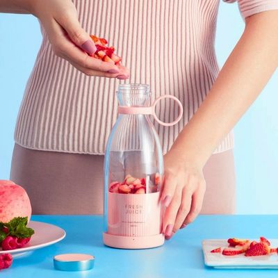 Personne mettant des morceaux de fruits dans un mixeur portable.