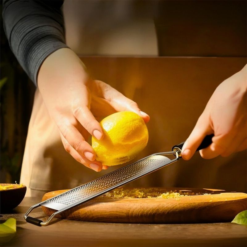 Personne qui utilise un zesteur pour récupérer des zestes de citron au-dessus d'une planche en bois.