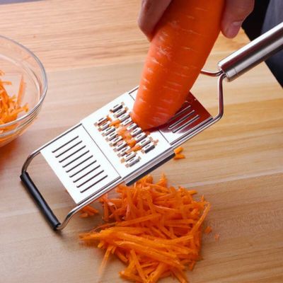 Personne utilisant une râpe à légumes manuelle inox interchangeal'ine pour râper une carotte.
