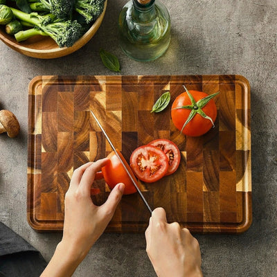 Planche à découper bois posée sur une table et utilisé par une personne pour couper ne tommate.