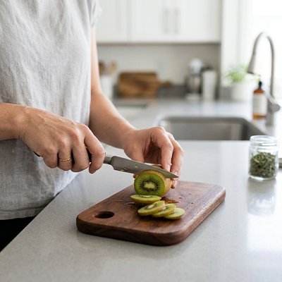 Planche à découper bois utilisée par une femme qui coupe des tranches de kiwis