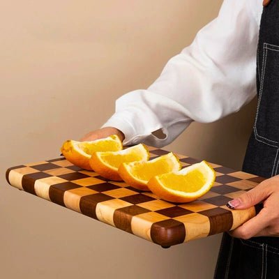 Planche à découper en bois en motif damier tenue par personne avec quart de citron dessus.