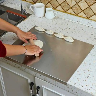 planche à découper en inox sur plan de travail avec personne pétrissant pâte