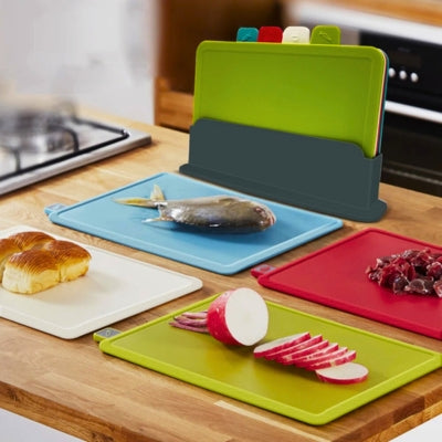 Planche découper posé sur une table dans le support de rangement devant les 4 planches disposées avec leurs aliments de prédilection posée dessus.