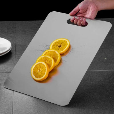 planche à découper inox tenue par une personne avec des morceaux d'orange qui ne glissent pas.