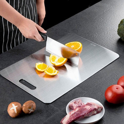 planche à découper inox utilisée par une personne pour couper une orange.