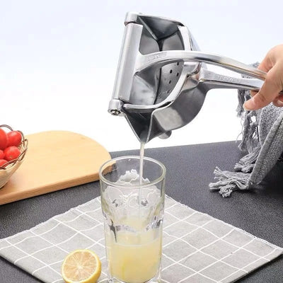 Presse agrume manuel tenu par une main d'une personne pour verser directement dans un verre du jus de fruit, en dessous un torchon avec une citron coupé en deux.