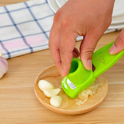 Presse ail utilisé par une personne au-dessus d'une coupelle, on voit des gousses d'ail dans la coupelle ainsi que l'ail pressé.