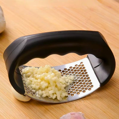 Presse ail tenu posé sur une table au-dessus d'une gousse d'ail, on voit également de l'ail déjà pressé sur l'appareil.