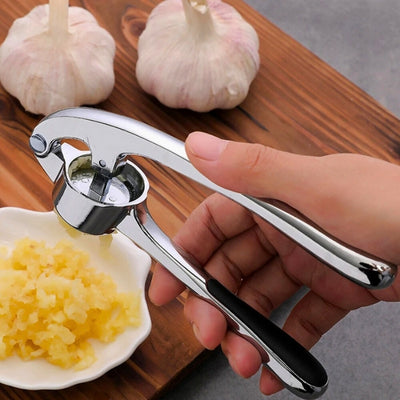 presse ail utilisé par une personne pour presser une gousse d'ail au-dessus d'une coupelle remplie de purée d'ail posée sur une planche à découper.
