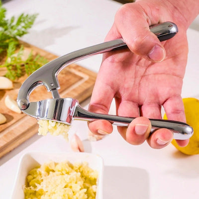 presse ail utilisé par une personne pour presser une gousse d'ail au-dessus d'une coupelle remplie de purée d'ail, en arrière-plan une planche à découper.