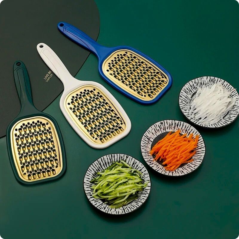 Râpe à carottes posée sur une table à côté assiette de légumes râpés.