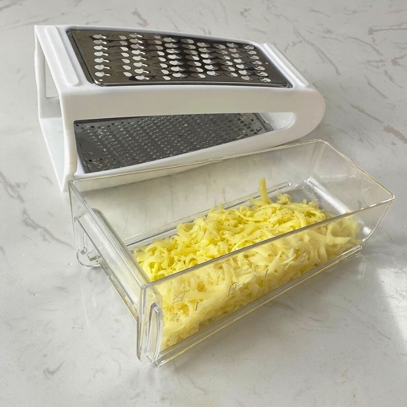 Râpe à fromage posée sur une table à côté de son réservoir rempli de fromage râpé.