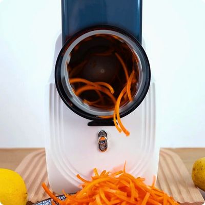 Râpe à légumes électrique posée sur une table avec des carottes râpées qui sortent de l'appareil.